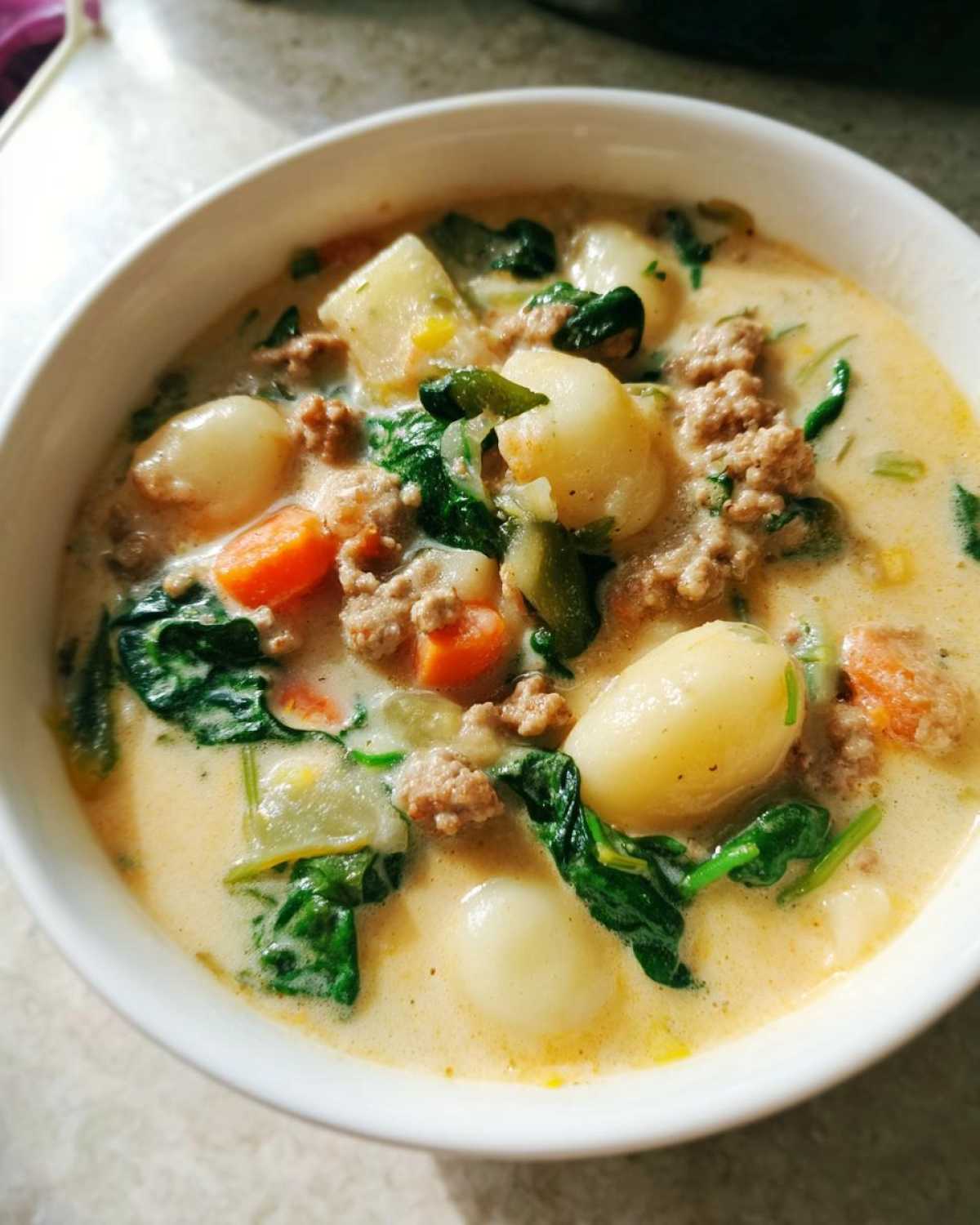 Close-up of a bowl of creamy sausage gnocchi soup with chunks of sausage, potatoes, carrots, and spinach.