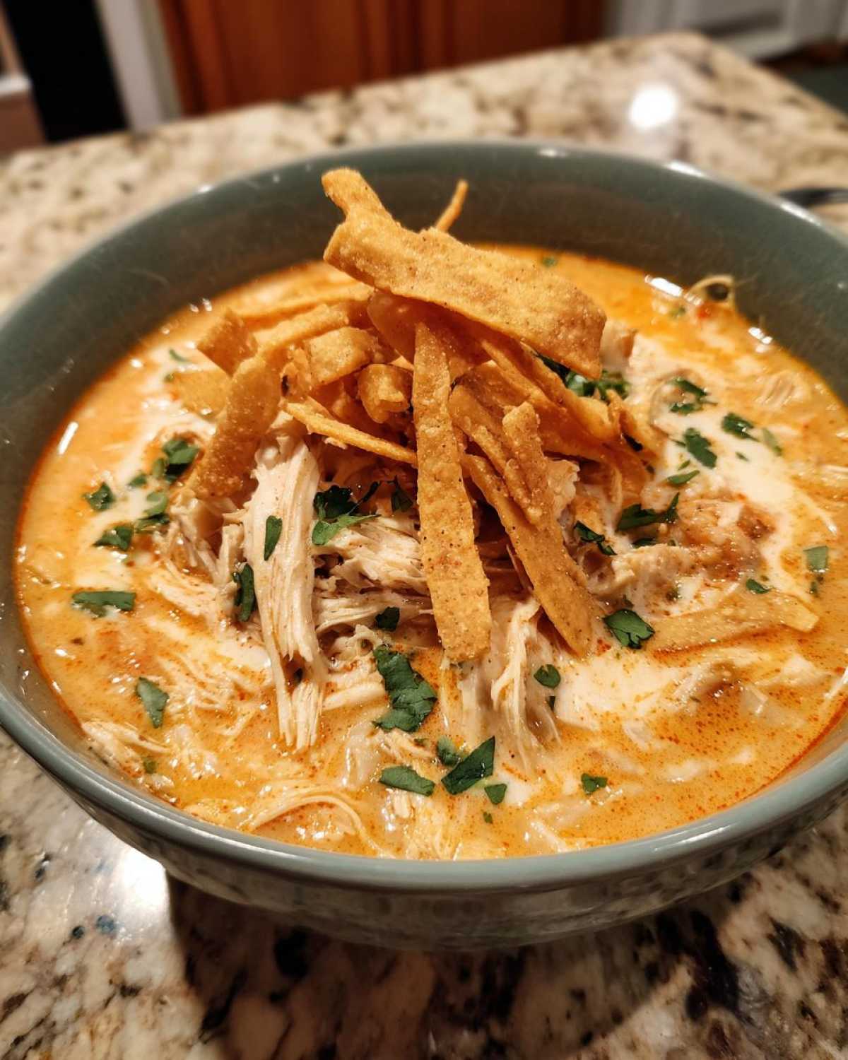Close-up of a bowl of creamy tortilla soup recipe, topped with shredded chicken, crispy tortilla strips, and cilantro.