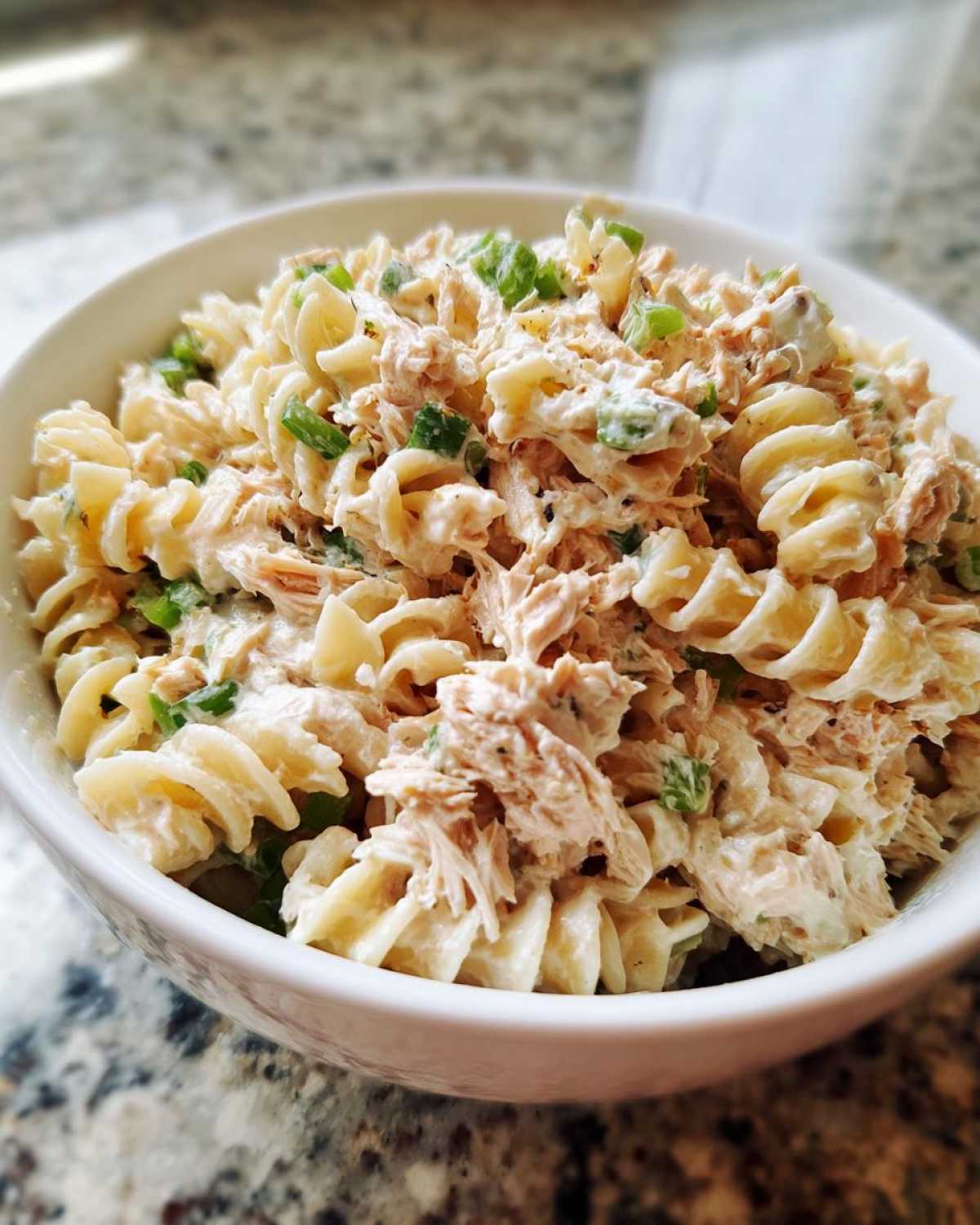 Close-up of creamy Tuna Pasta Salad made with rotini pasta, tuna, and green onions in a white bowl.