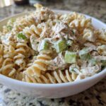 Close-up of creamy tuna pasta salad made with rotini pasta and celery chunks in a white bowl.
