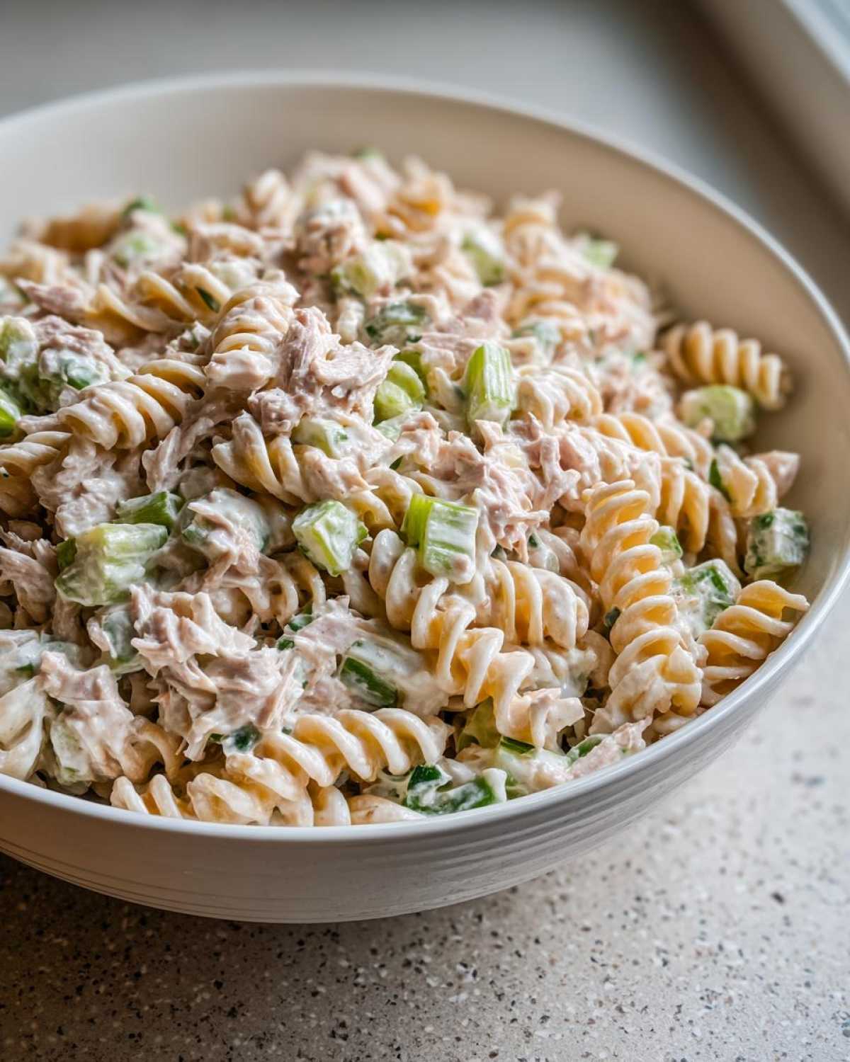 Close-up of creamy tuna pasta salad made with rotini pasta and chopped celery in a white bowl.