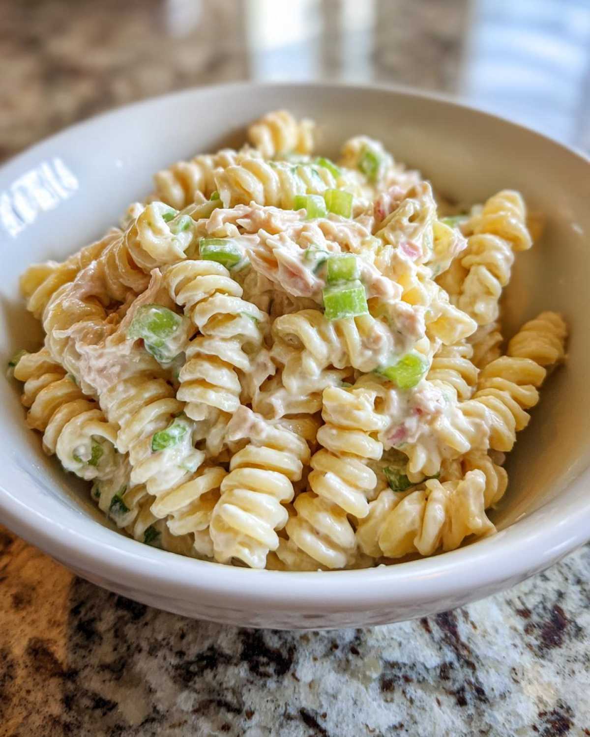 Close-up of creamy Tuna Pasta Salad made with rotini pasta and chopped green celery in a white bowl.