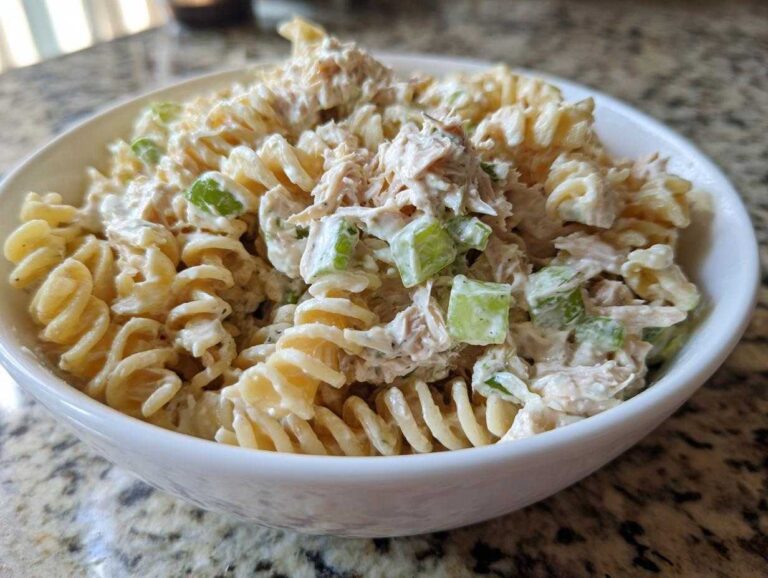 Close-up of creamy tuna pasta salad made with rotini pasta and celery chunks in a white bowl.