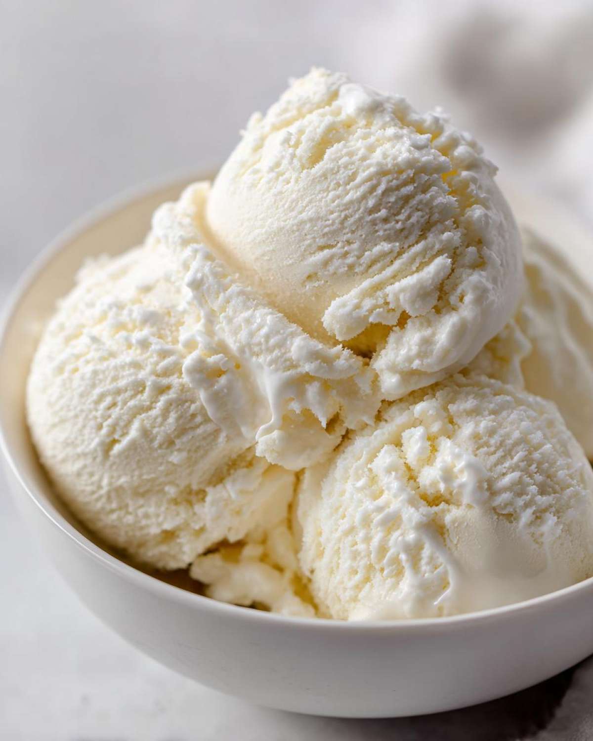 Close-up of three scoops of creamy white protein ice cream served in a small white bowl.