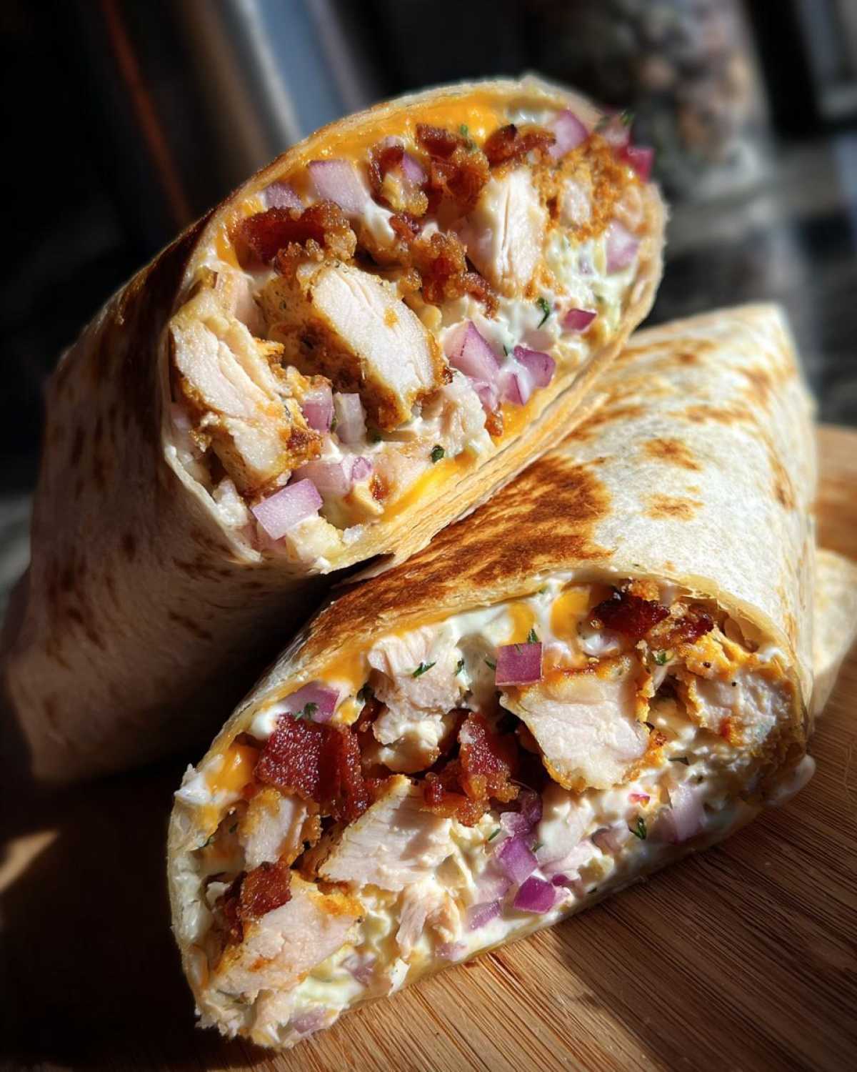 Close-up of a chicken bacon ranch wrap cut in half, showing chunks of chicken, bacon, red onion, and ranch dressing.