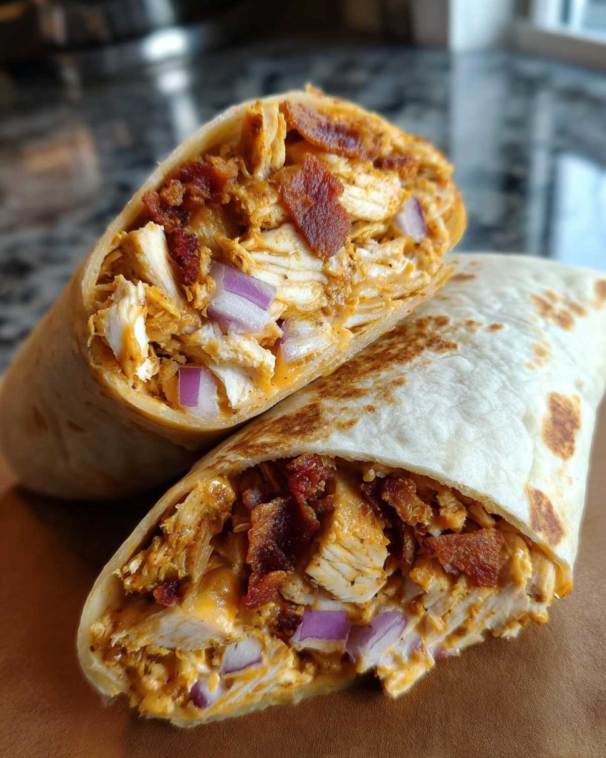 Close-up of a chicken bacon ranch wrap cut in half, showing shredded chicken, bacon, and red onion inside a toasted tortilla.