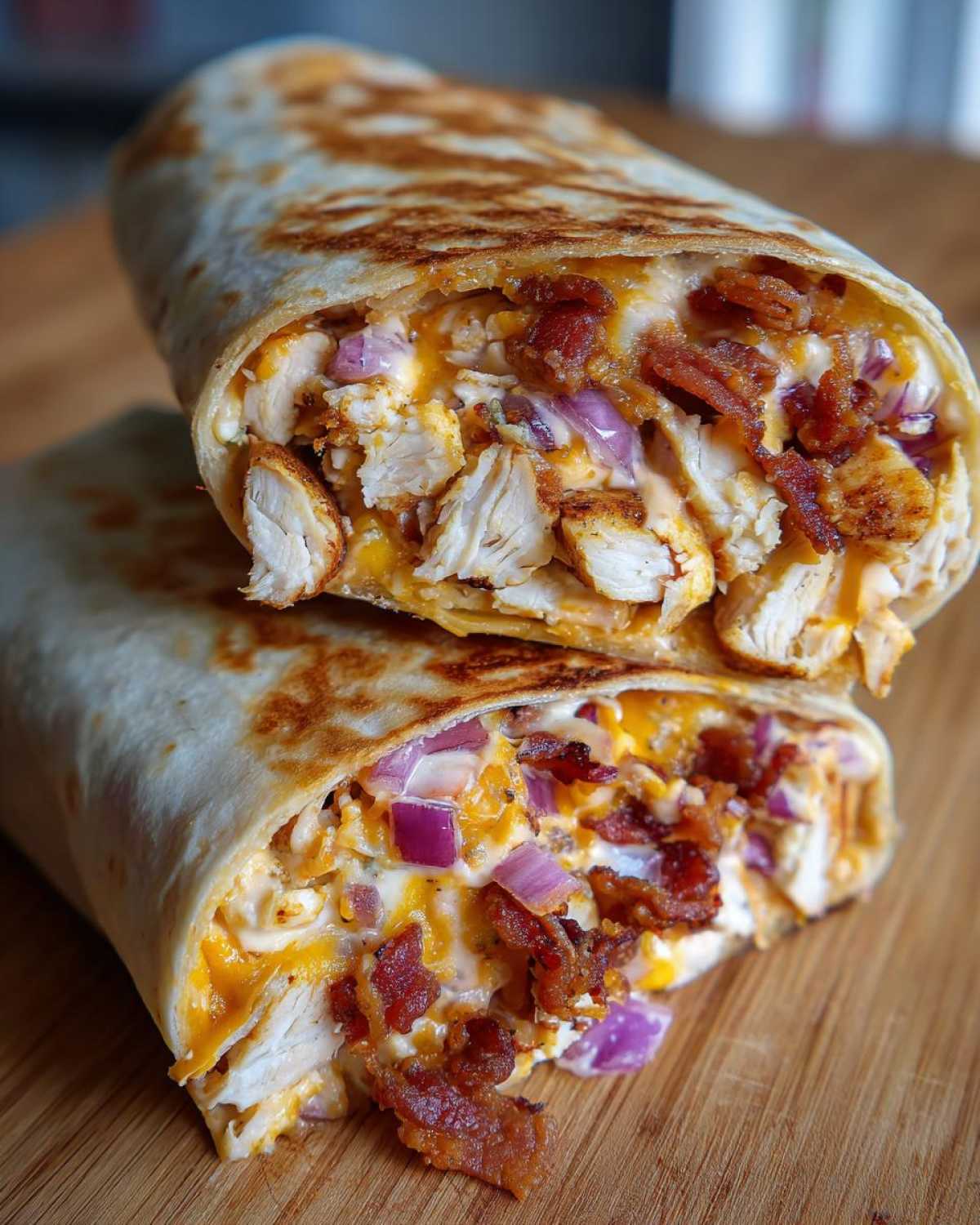 Close-up of a crispy chicken bacon ranch wrap cut in half, showing chicken, bacon, cheese, and red onion filling.
