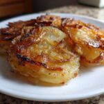 Close-up of golden brown, crispy fried potatoes stacked on a white plate, showing caramelized edges.
