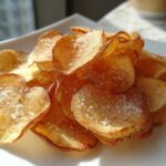 A pile of golden brown, crispy homemade potato chips seasoned generously with coarse sea salt.