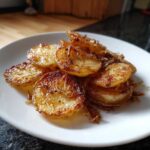Close-up of golden brown, crispy sliced fried potatoes seasoned with pepper, served on a white plate.