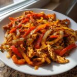 Close-up of seasoned chicken strips mixed with sliced red and orange bell peppers and onions, ready to serve for crockpot chicken fajitas.