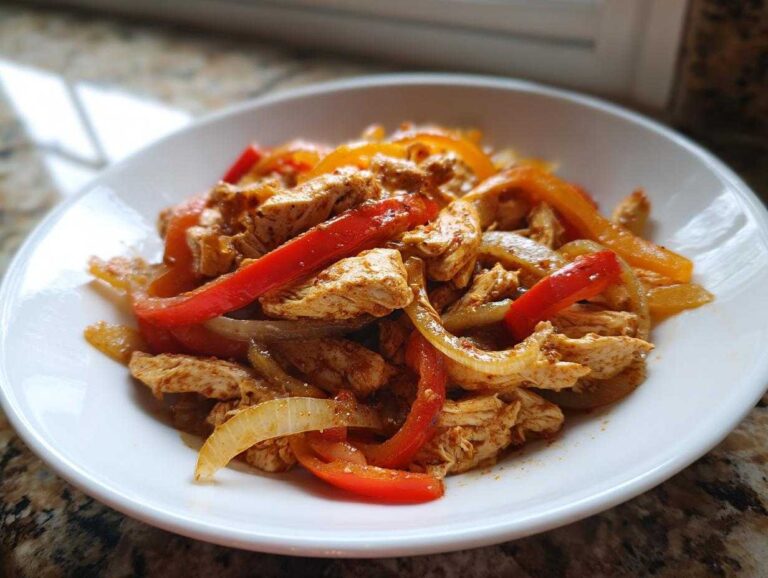 Close-up of seasoned chicken strips mixed with sautéed red and orange bell peppers and onions, ready to eat crockpot chicken fajitas.