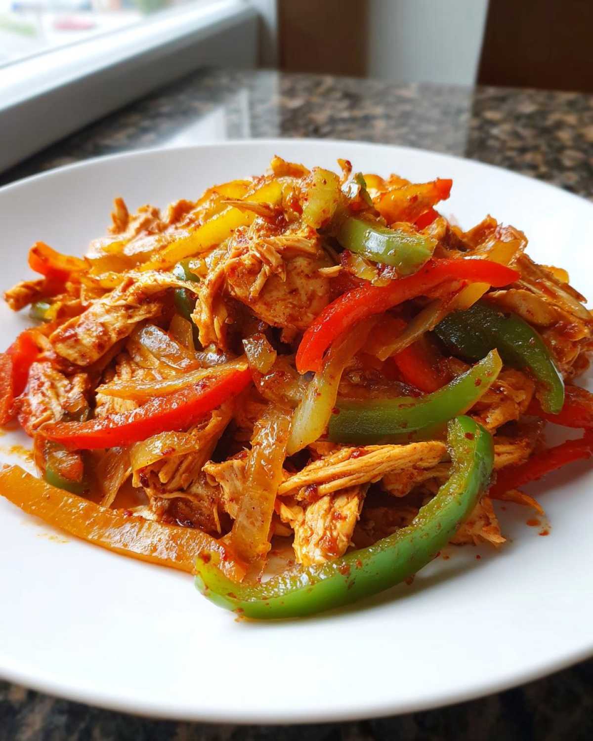 A white plate piled high with shredded crockpot chicken fajitas mixed with colorful sautéed bell peppers and onions.