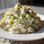 A generous serving of creamy dill pickle chicken salad, featuring chunks of chicken and bright green pickles, piled high on a white plate.