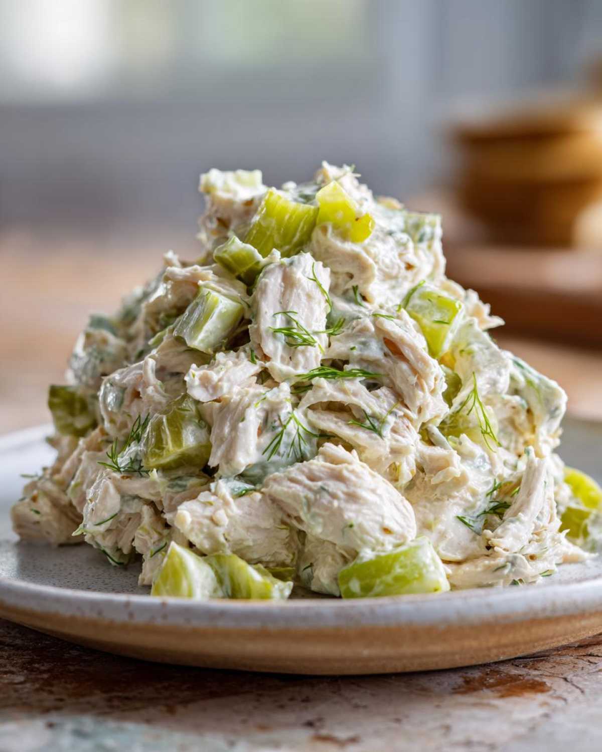 A close-up of a generous mound of creamy dill pickle chicken salad featuring shredded chicken, chunks of pickles, and fresh dill.