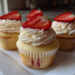 Three delicious strawberry cupcakes topped with white frosting and fresh strawberry slices, ready to eat.