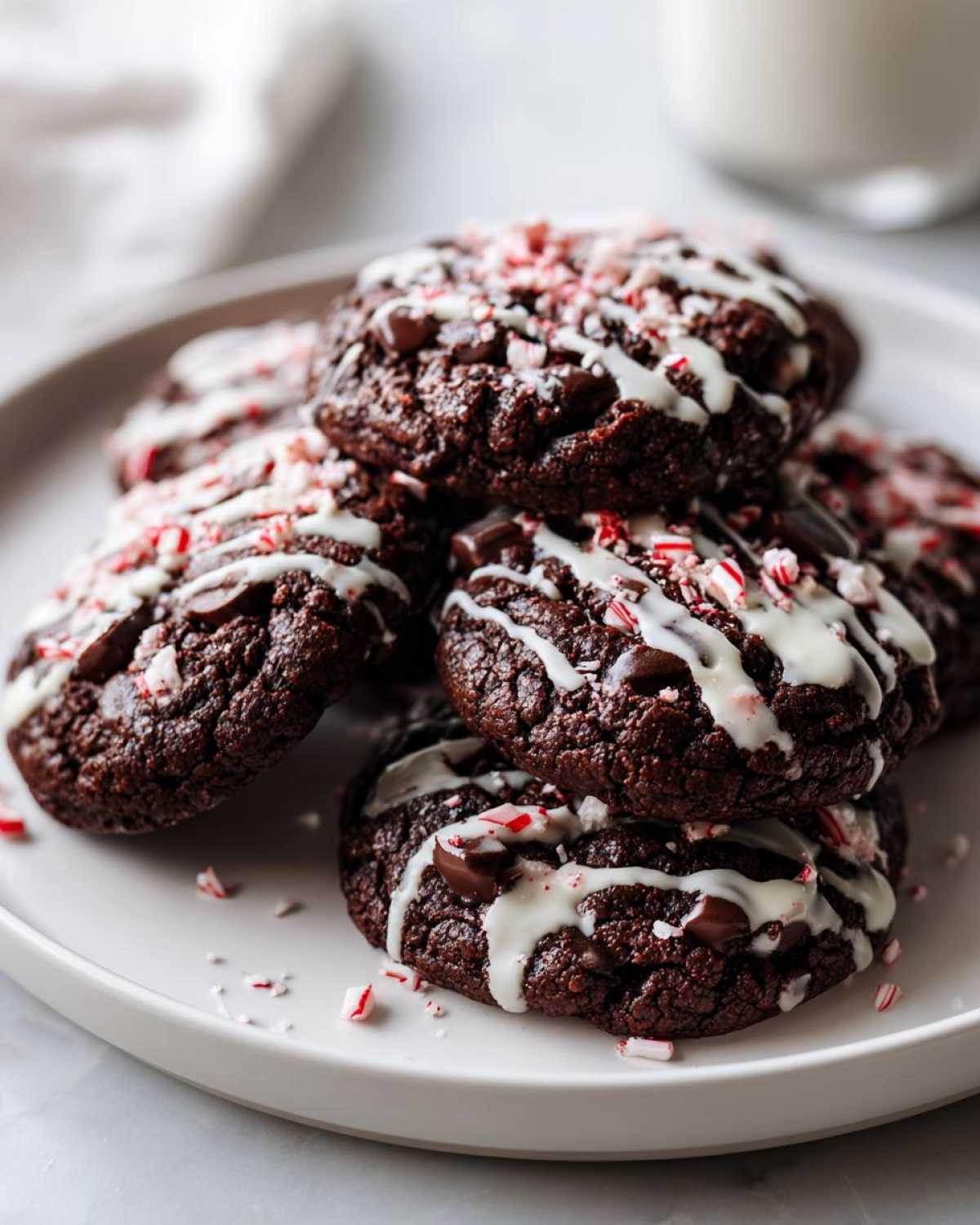 A stack of rich, dark double chocolate peppermint cookies drizzled with white chocolate and topped with crushed candy canes.