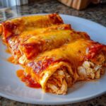 Close-up of three easy chicken enchiladas covered in melted cheese and red sauce, showing shredded chicken filling.
