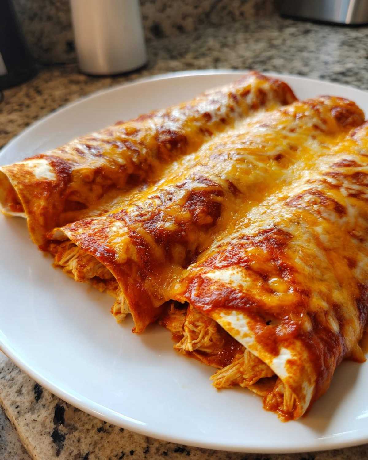 Three rolled tortillas filled with shredded chicken, covered in red sauce and melted cheese for easy chicken enchiladas.