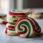 A stack of colorful red and green pinwheel cookies coated in sparkling sugar on a white marble surface.