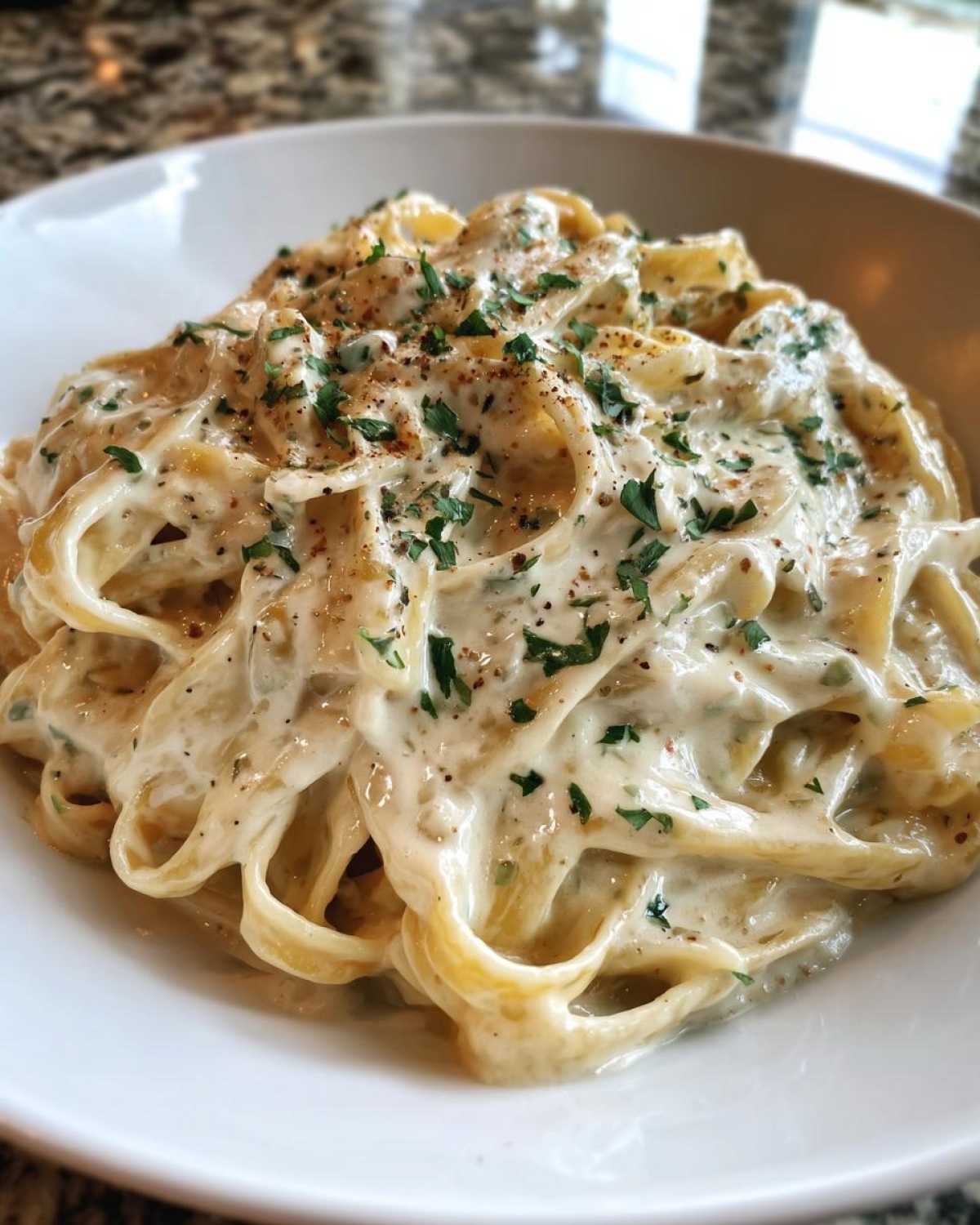 Close-up of fettuccine pasta coated in creamy Olive Garden Alfredo sauce, topped with black pepper and parsley.