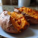 Two halves of a fluffy baked sweet potatoes showing bright orange interior on a white plate.