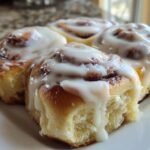 Close-up of four fluffy cinnamon rolls generously topped with dripping white cream cheese icing.