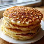 A tall stack of four fluffy pancakes showing a beautiful golden-brown honeycomb surface texture.