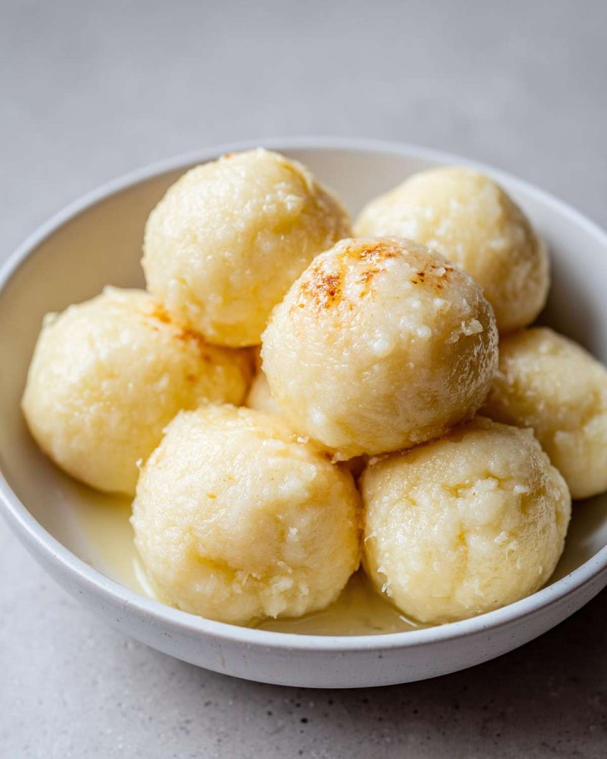 Close-up of several fluffy potato dumplings served in a white bowl, glistening with melted butter.