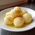 A white bowl filled with several golden brown potato dumplings soaking in melted butter.