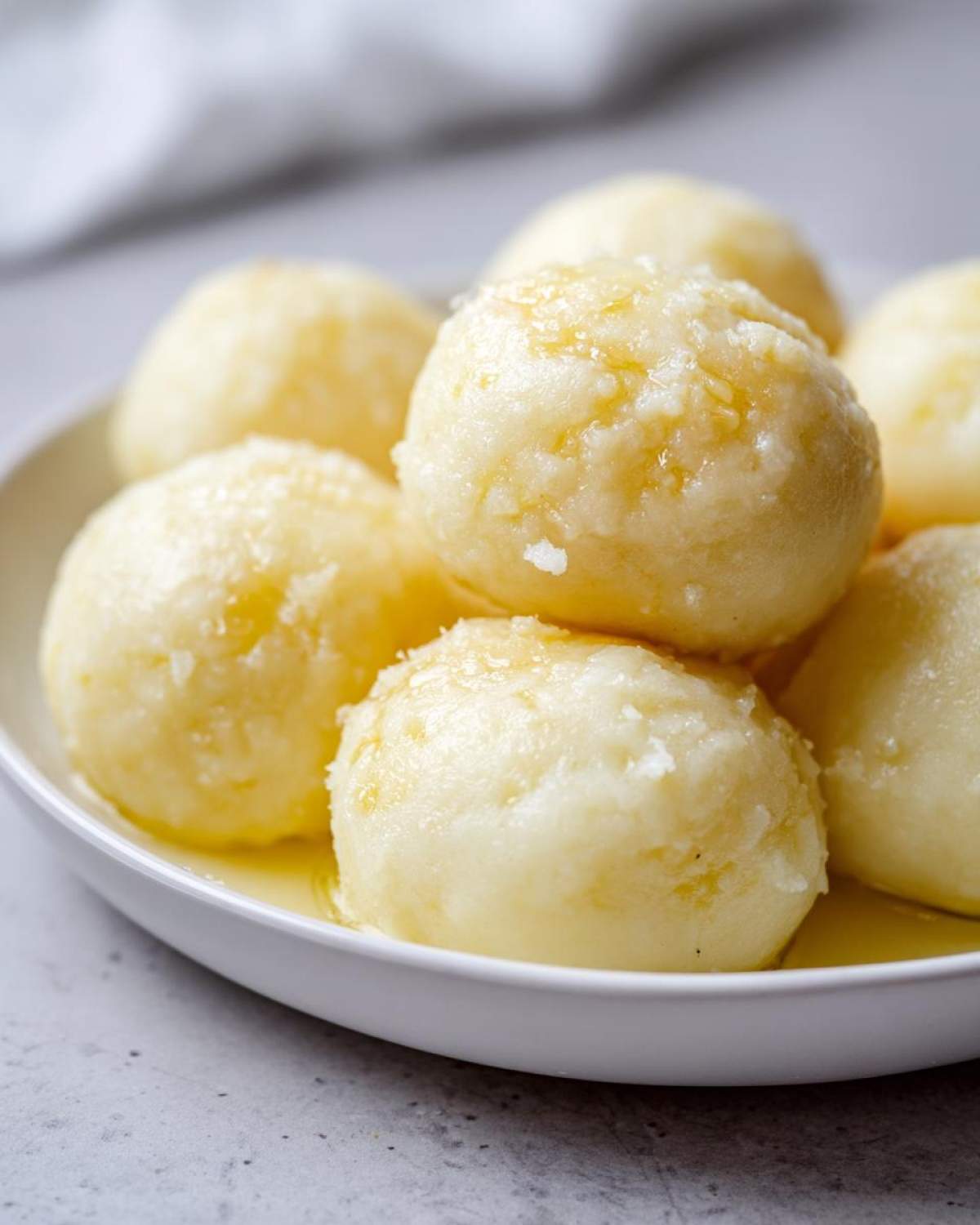 Close-up of several fluffy potato dumplings served in a white bowl and glistening with melted butter.