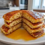 A stack of four thick sourdough pancakes, cut in half to show the fluffy interior, drizzled with maple syrup.