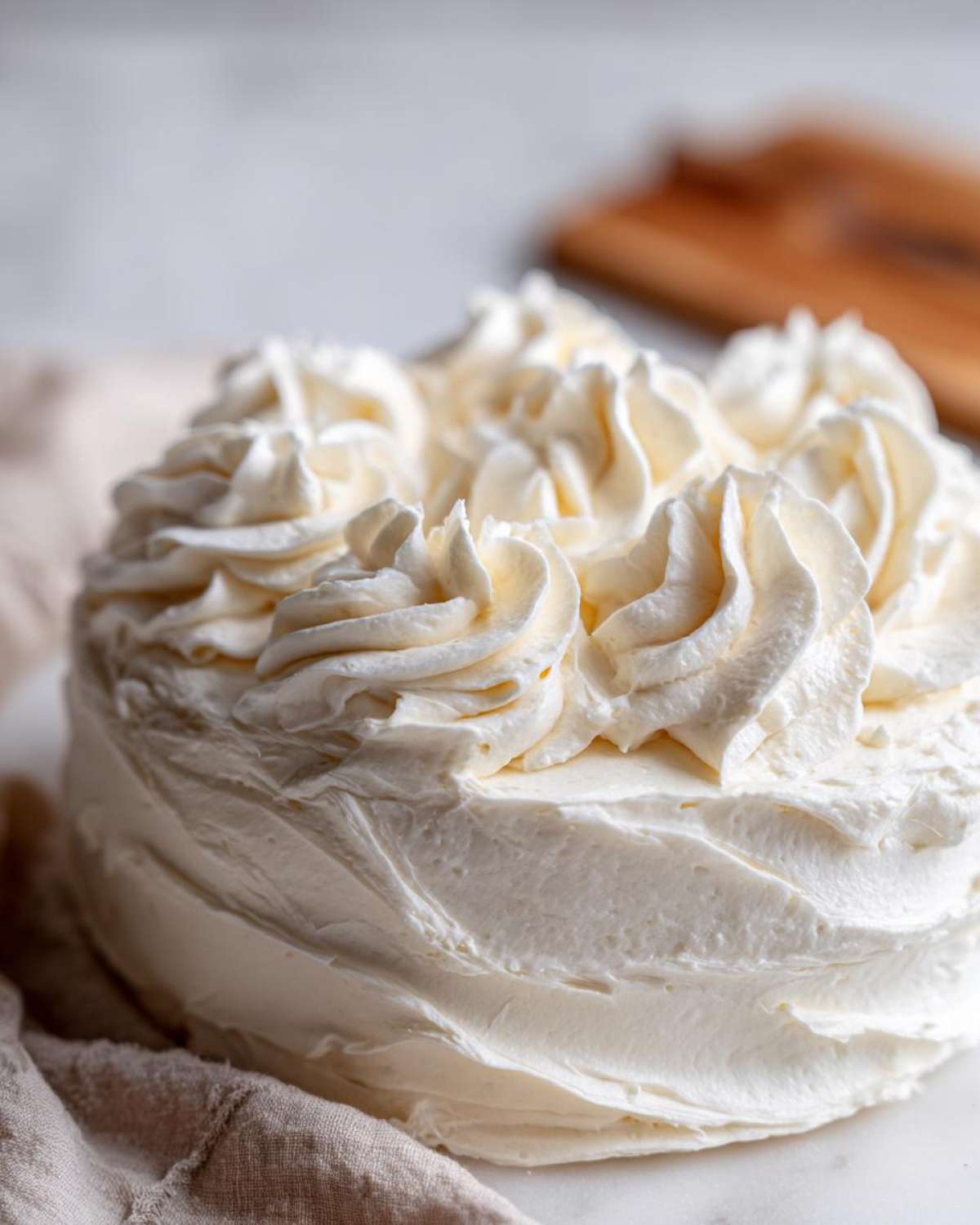 A close-up of a round cake generously frosted with swirls of creamy vanilla buttercream.