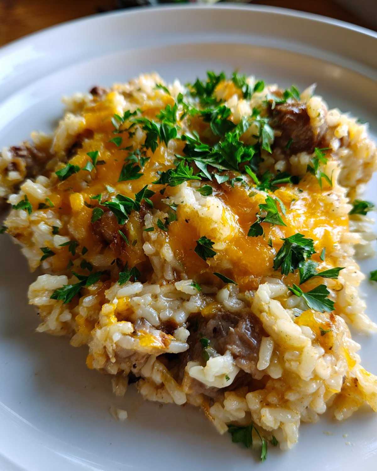 Close-up of a serving of french onion butter rice topped with melted cheddar cheese and fresh parsley.