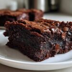 Close-up of a fudgy, dark chocolate slice of black bean brownies showing melted chocolate chips on a white plate.
