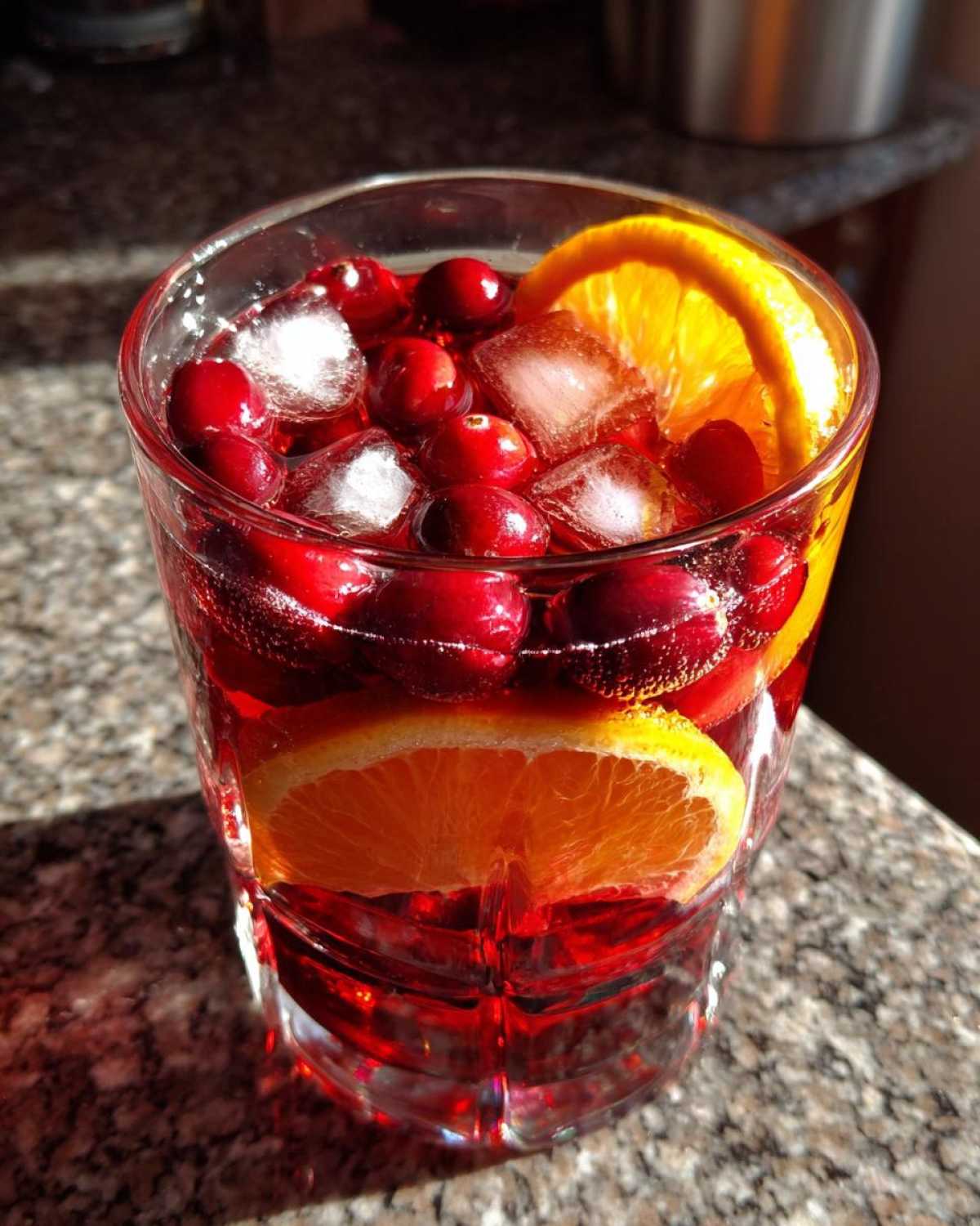 Close-up of a glass filled with red holiday sangria, ice cubes, fresh cranberries, and orange slices.