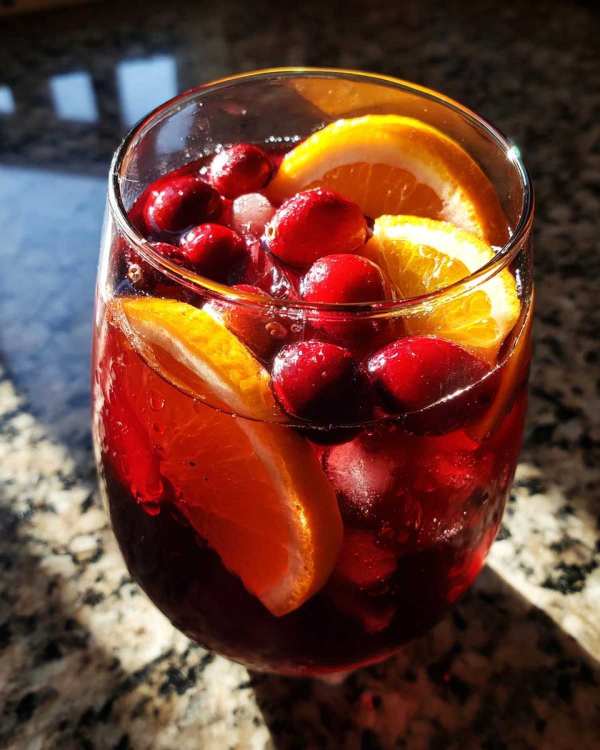 Close-up of a glass filled with deep red holiday sangria, garnished with fresh cranberries and bright orange slices.