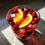 Close-up of a glass filled with vibrant red holiday sangria, garnished with fresh cranberries, orange slices, and ice.