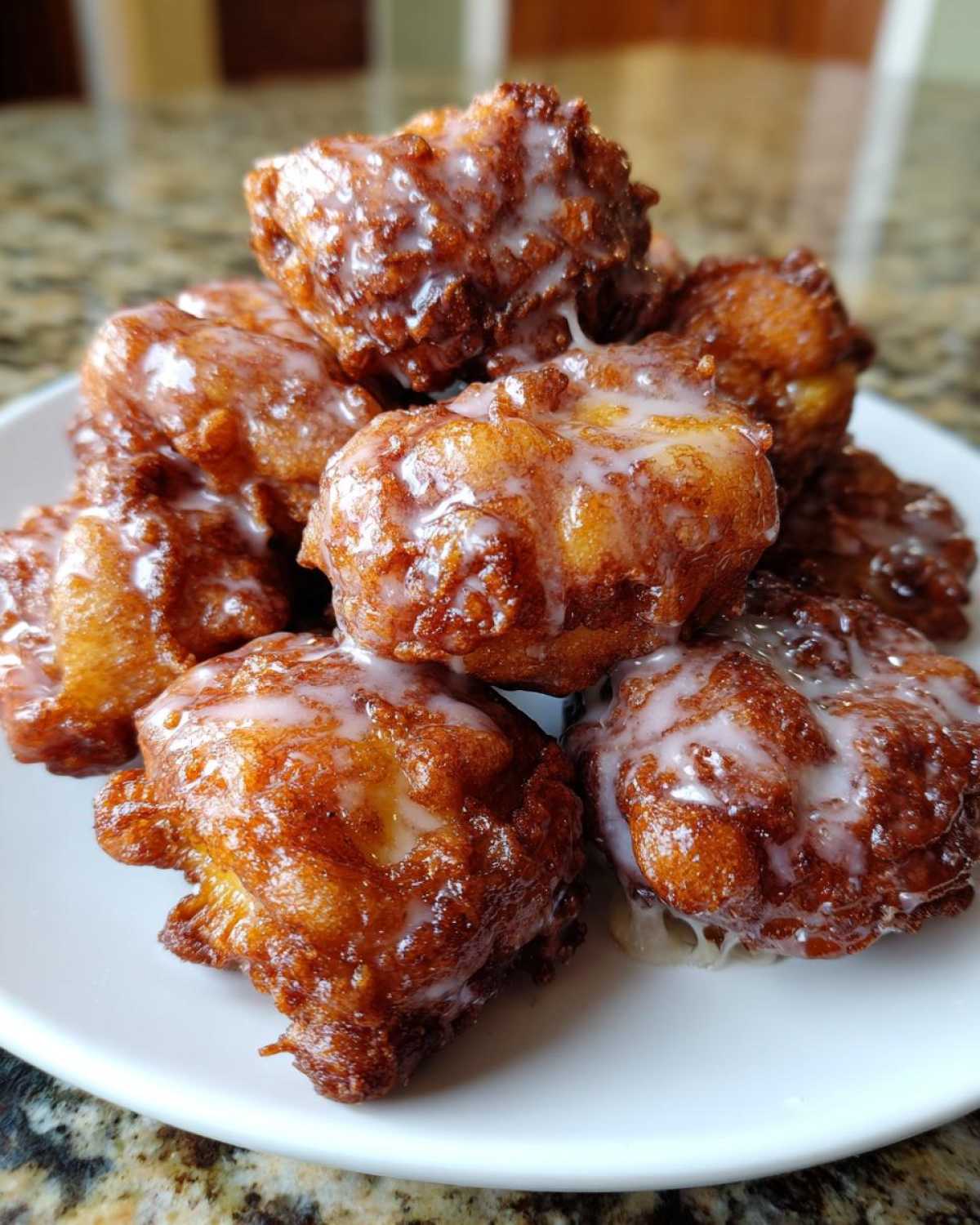 A pile of golden brown, freshly fried apple fritter pieces drizzled with a sweet white glaze.