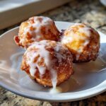 Close-up of three golden brown baked apple fritters heavily drizzled with white vanilla glaze.