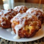 Close-up of four golden brown baked apple fritters generously drizzled with white vanilla glaze.