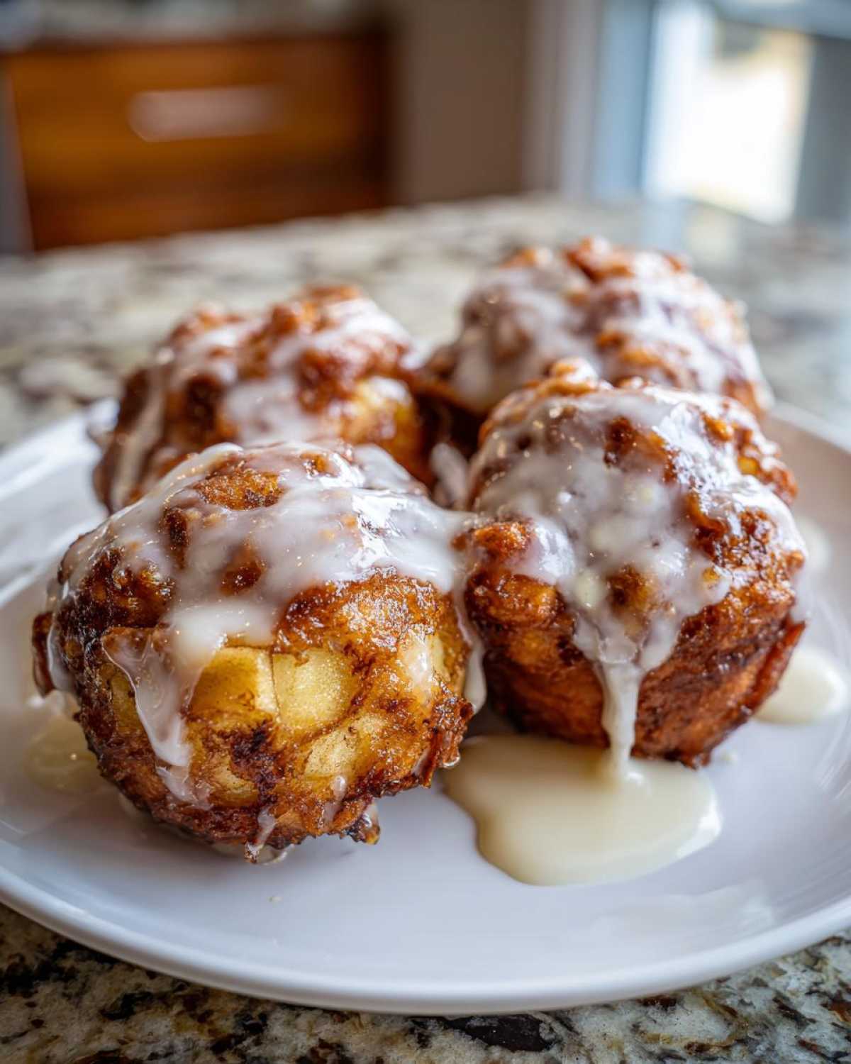 Four golden brown baked apple fritters generously drizzled with white vanilla glaze, resting on a white plate.