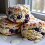 A stack of three fluffy blueberry scones topped with thick white icing dripping down the sides.