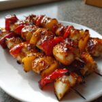 Close-up of grilled chicken skewers glazed with a sticky sauce, interspersed with yellow peppers and red peppers.