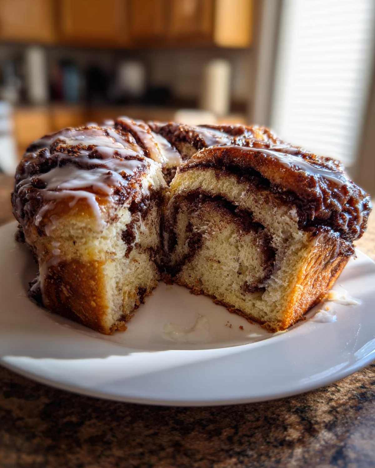 A freshly baked chocolate babka, drizzled with white icing, with one slice cut out revealing the swirled interior.
