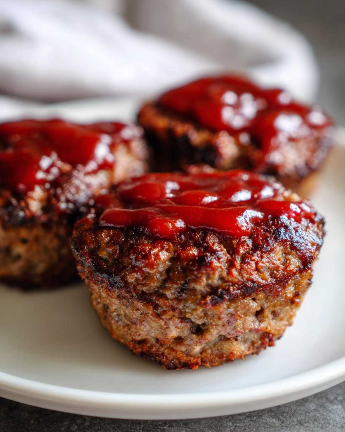 Three perfectly baked mini meatloaf portions topped with a thick layer of bright red glaze, served on a white plate.