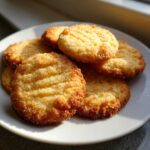 A stack of golden, sugar-coated 3-ingredient butter cookies resting on a white plate, illuminated by sunlight.