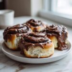 Close-up of four gooey chocolate cinnamon rolls heavily frosted and dripping with rich chocolate glaze.