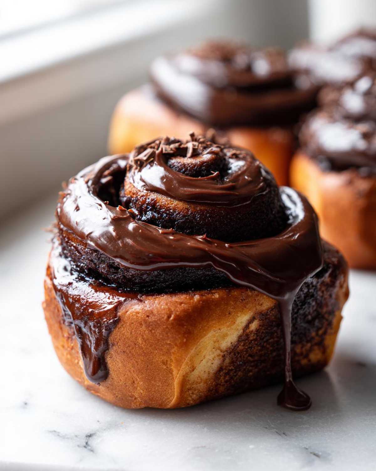Close-up of a gooey chocolate cinnamon roll topped with thick chocolate glaze and shavings.