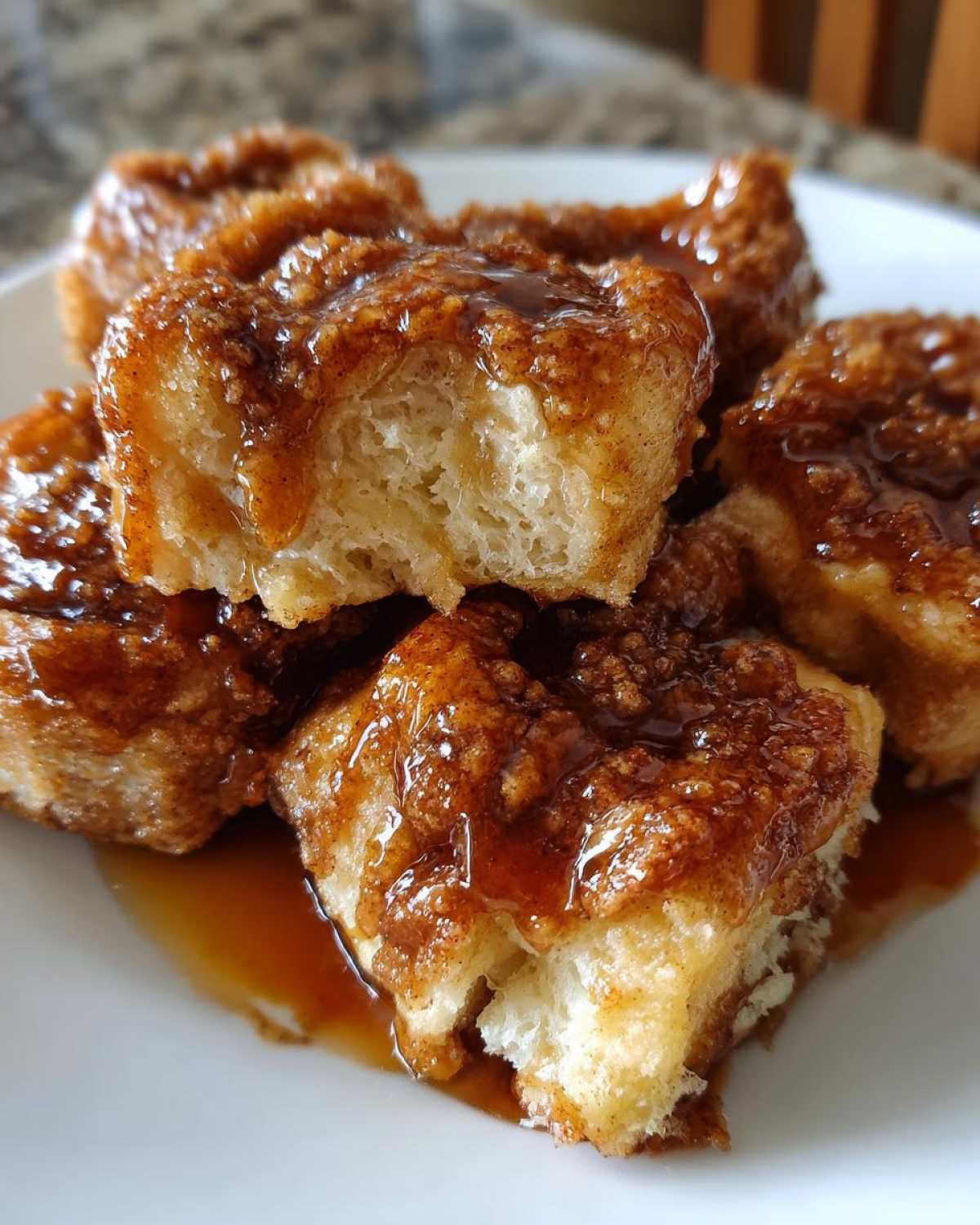 Close-up of several gooey cinnamon roll bites covered in rich caramel glaze on a white plate.